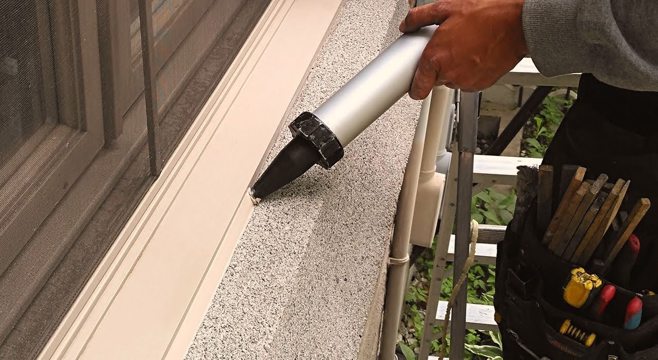 Person sealing window with a caulking gun.